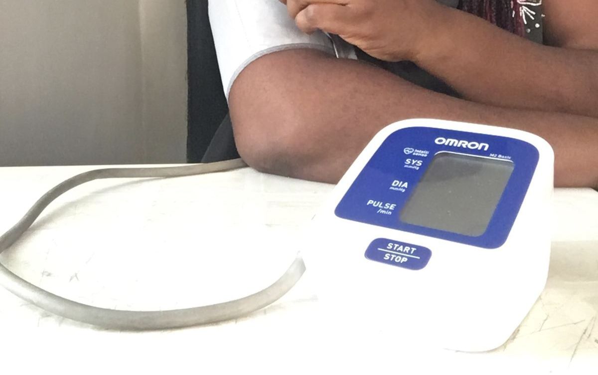 Oberarm mit Manschette und digitalem Blutdruckmessgerät auf einem Tisch